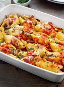 Stuffed shells topped with tomato sauce and cheese in a white baking dish.