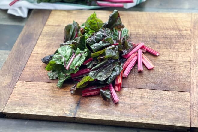 Raw Swiss chard roughly chopped on a wooden cutting board.