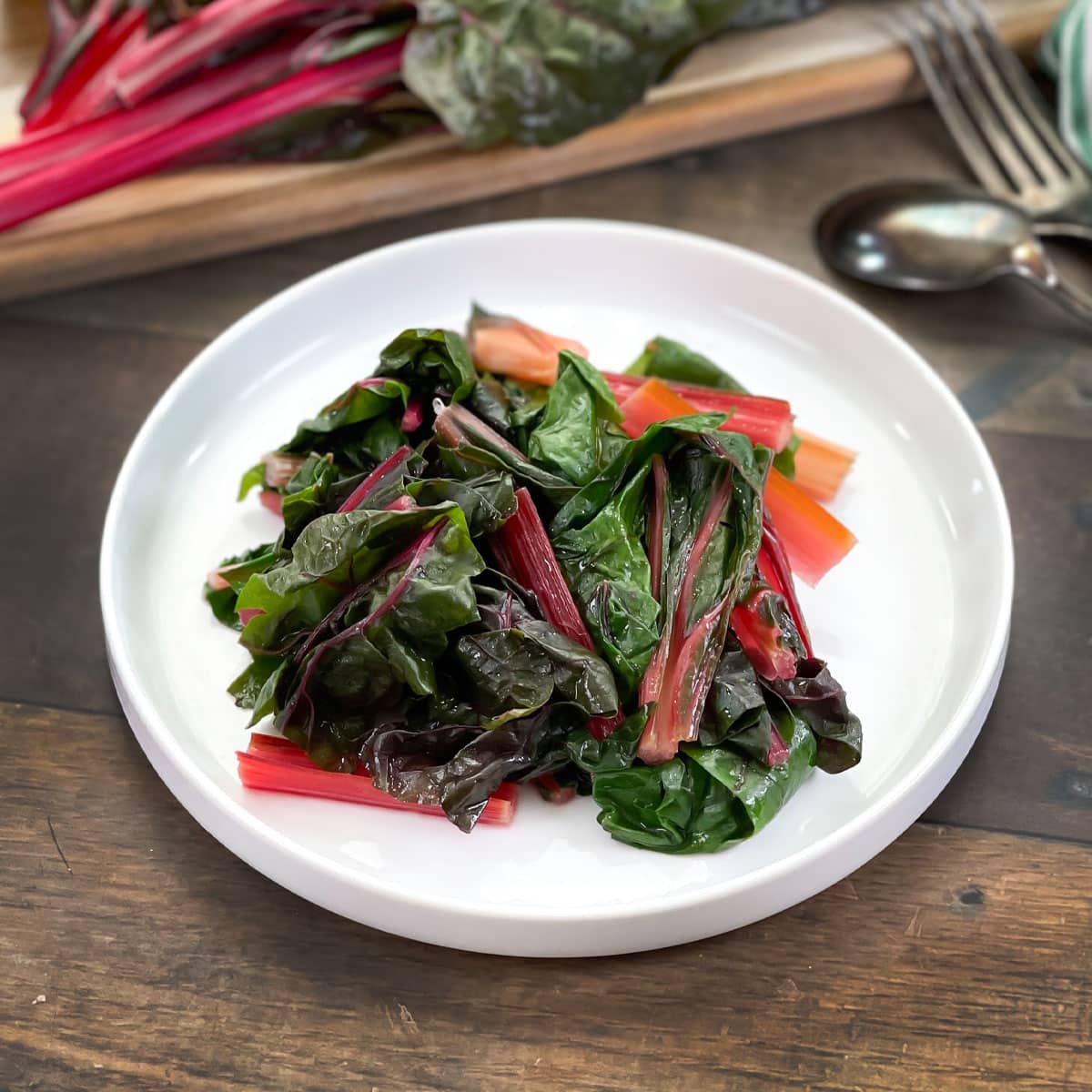 Sauteed Swiss chard on a white plate with raw chard in background.