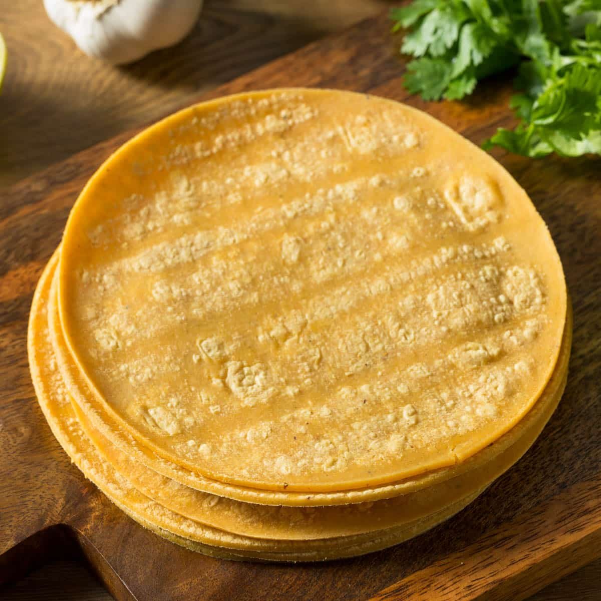 Stack of corn tortillas on a wooden board.