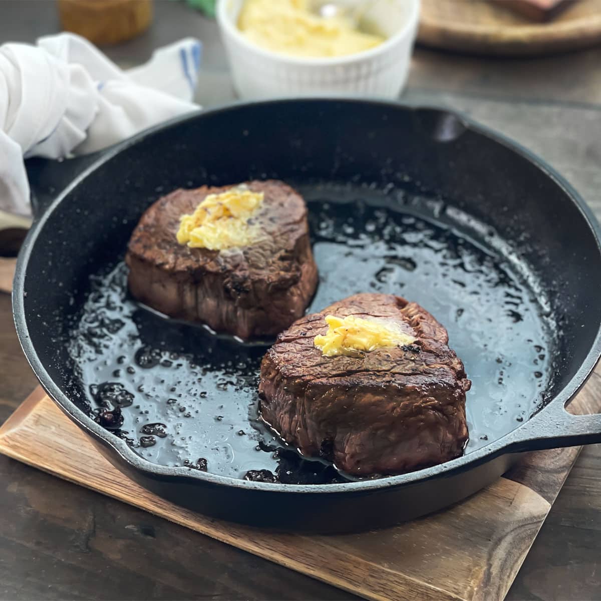 Two cooked filet mignon steaks in a cast iron skillet, topped with butter.