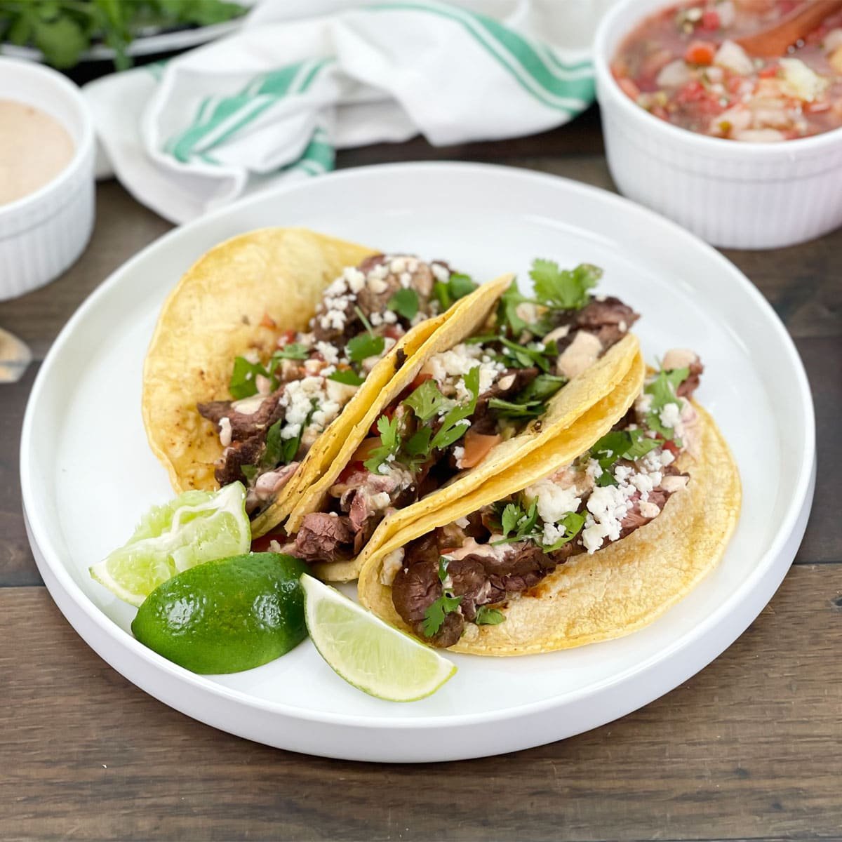 Carne asada tacos in soft corn tortillas, on a white plate with lime wedges.