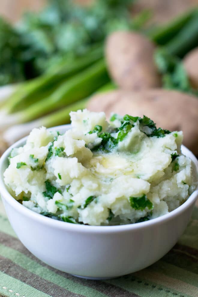 A bowl of colcannon, which is mashed potatoes mixed with wilted kale, topped with melting butter.