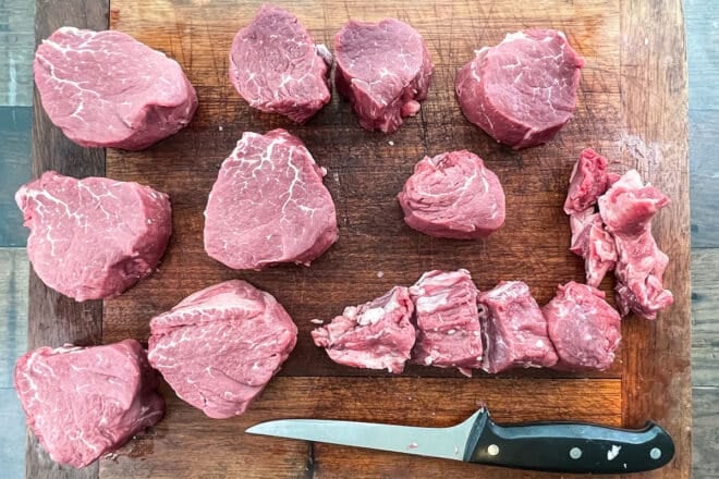 Center-cut and end-cut beef tenderloin steaks on wooden board.