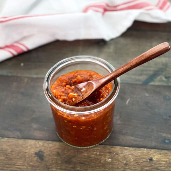 Glass jar of chili garlic sauce with small spoon.