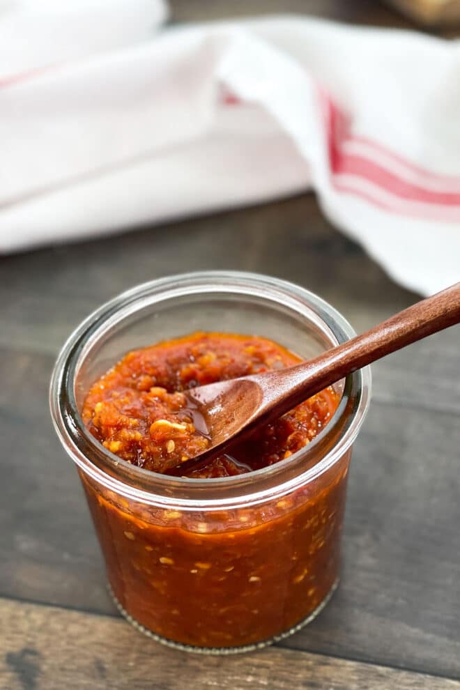 Glass jar of chili garlic sauce with small spoon.
