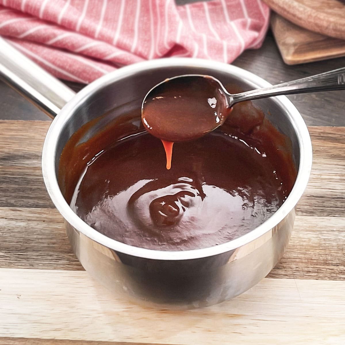 Rich brown espagnole sauce in a pot with spoon of sauce dripping over it.