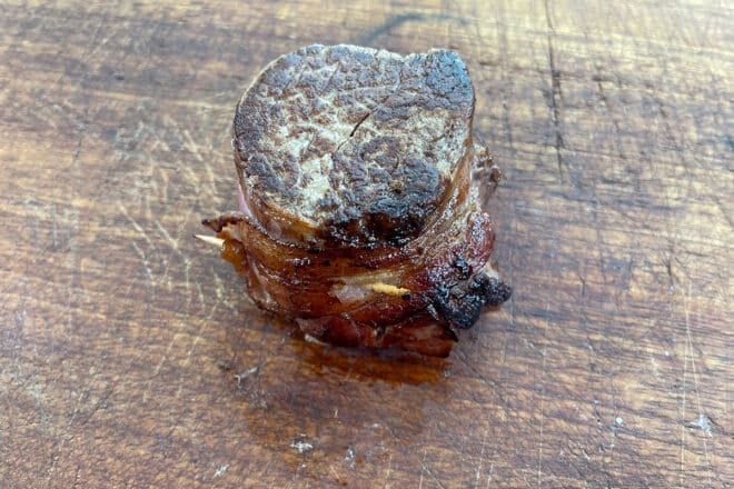 Cooked filet mignon with toothpick sticking out of the bacon.