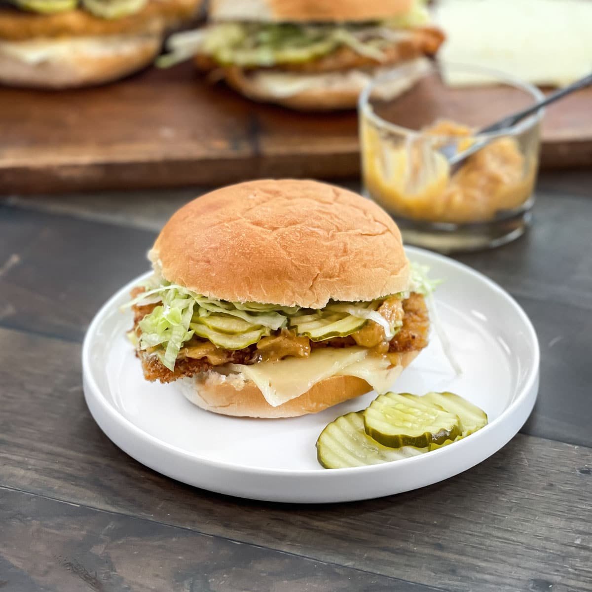 White plate with crispy chicken sandwich with cheese, lettuce, pickles and extra pickles on the plate.
