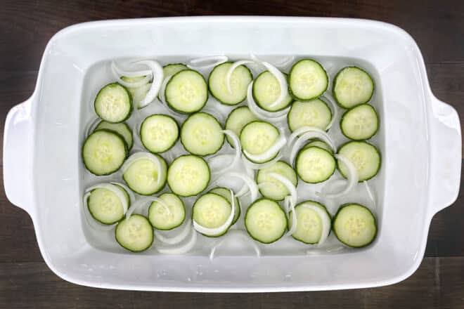 Overheard shot of cucumber onion salad marinating in a white casserole dish.