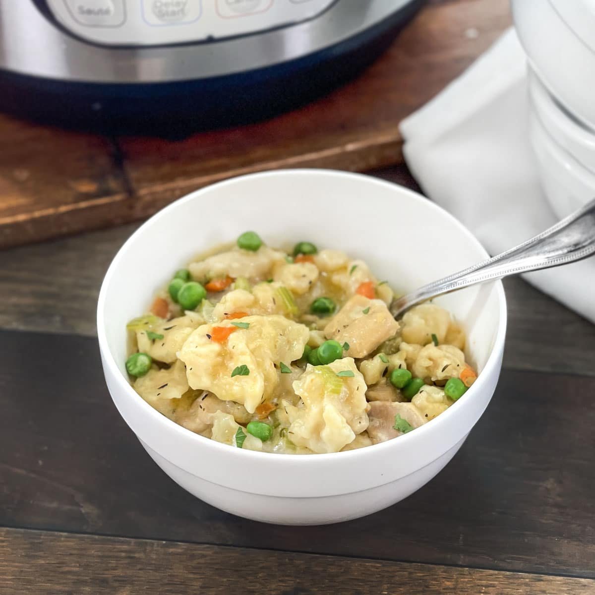 White bowl of chicken and dumplings in front of an Instant Pot.