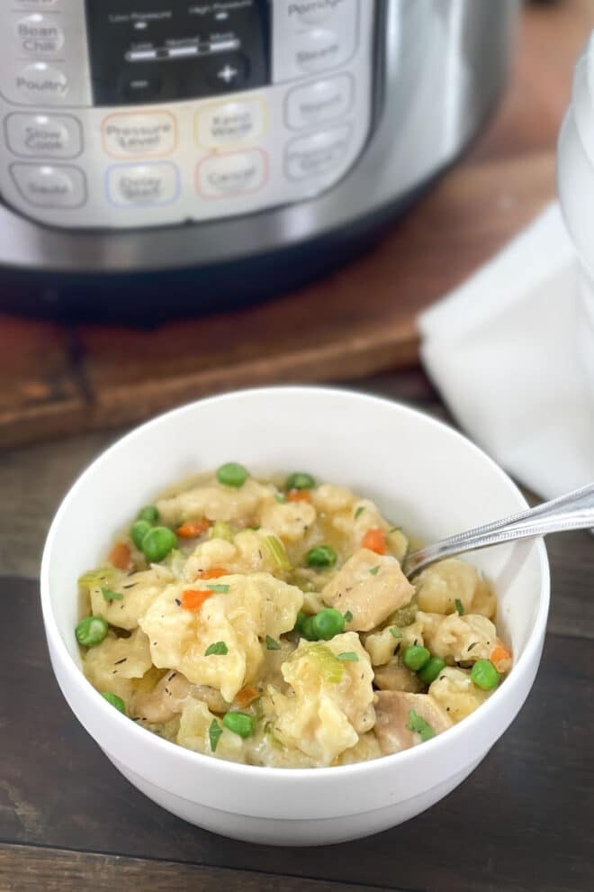 White bowl of chicken and dumplings in front of an Instant Pot.
