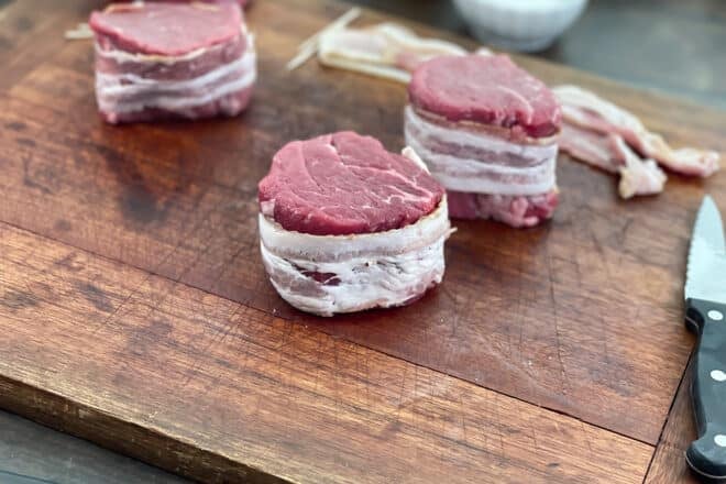 Raw bacon-wrapped filet mignon on a cutting board.