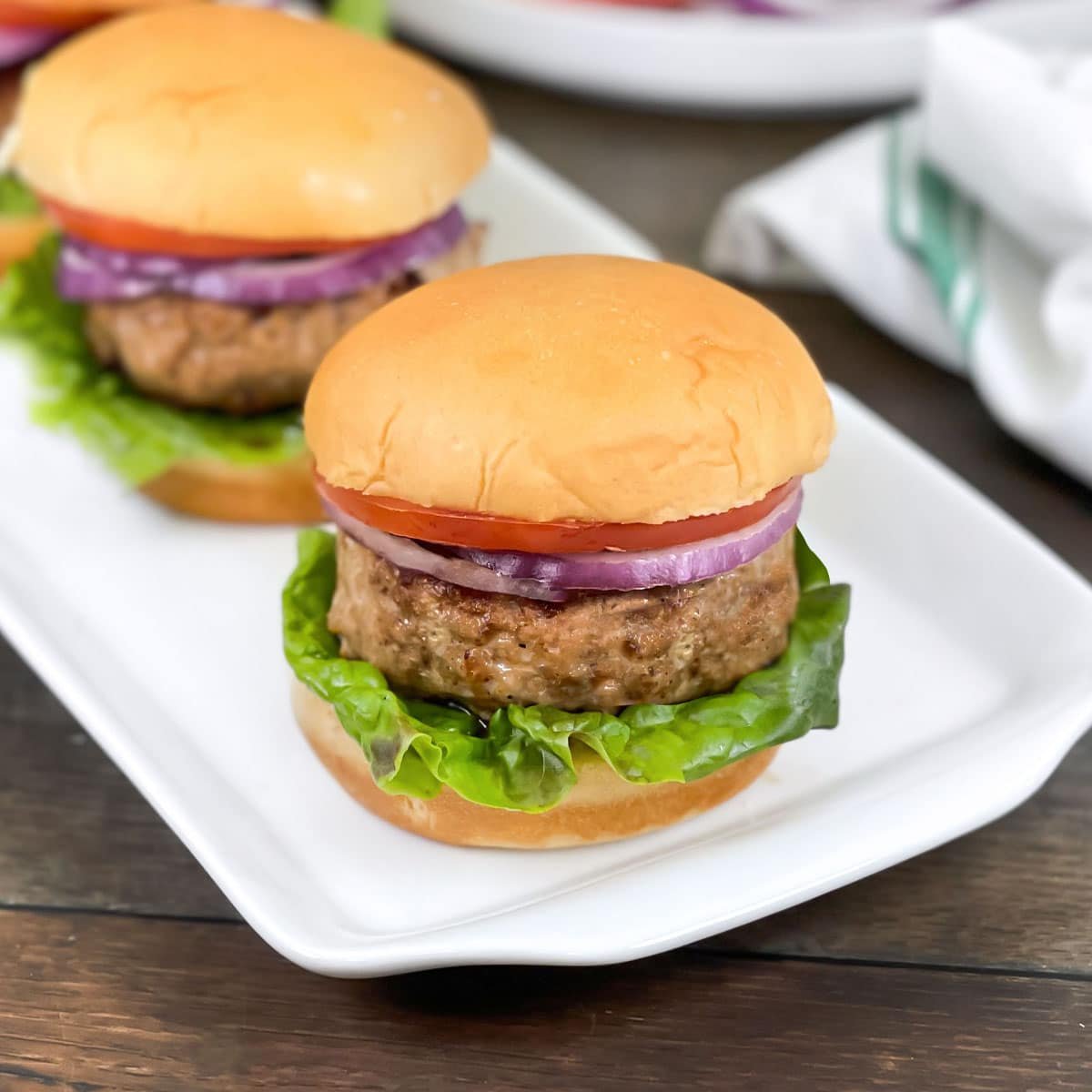 Chicken burgers with lettuce, red onion, and tomato on a rectangular white platter.