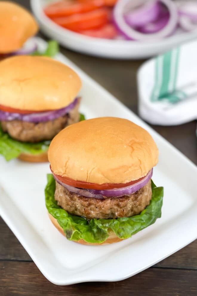 Chicken burgers with lettuce, red onion, and tomato on a rectangular white platter.