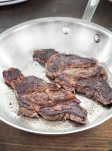 Cooked chuck eye steaks in a stainless steel pan.