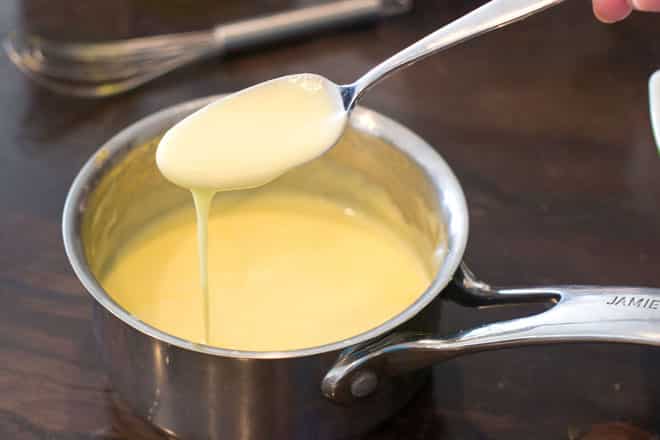 Classic Hollandaise sauce dripping from a spoon over a pan.