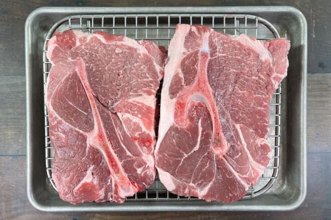 Two large, raw, bone-in pork steaks.