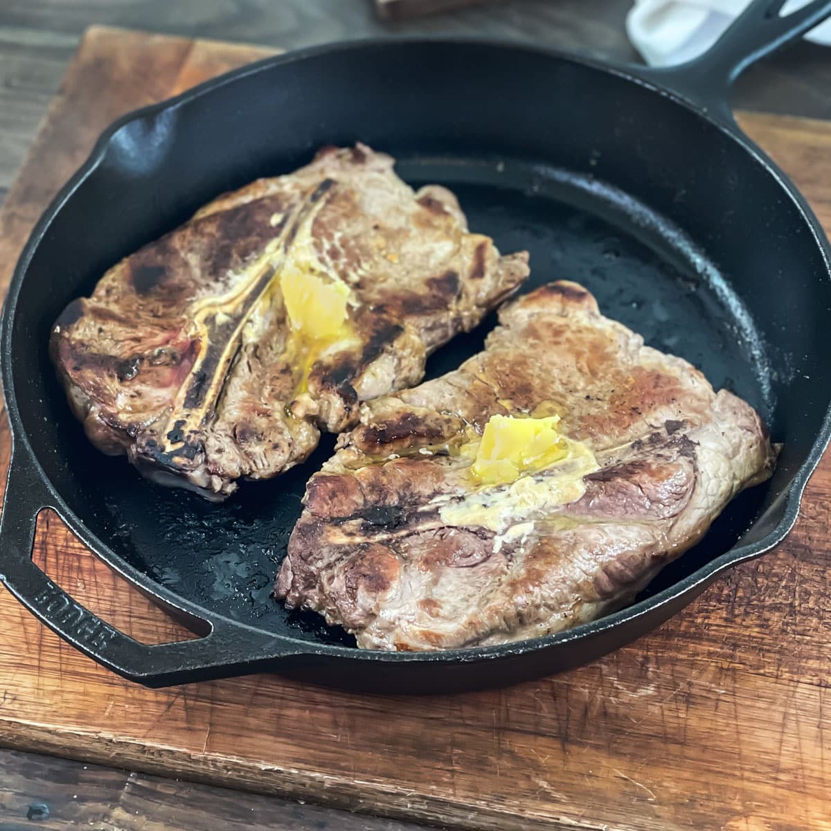 Large pork steaks in a cast iron skillet with pats of butter on top.