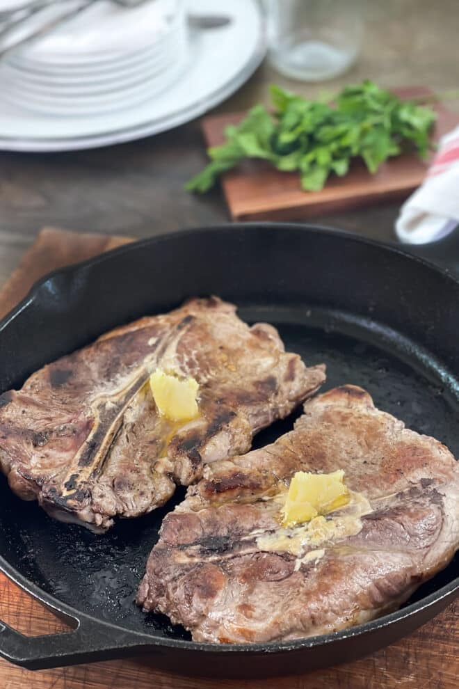 Large pork steaks in a cast iron skillet with pats of butter on top.