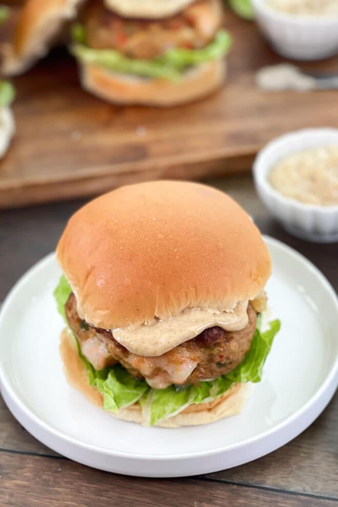 Shrimp burger with spiced mayo and lettuce on a white plate.