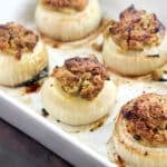 Whole baked onions filled with stuffing mixture in a white casserole dish.
