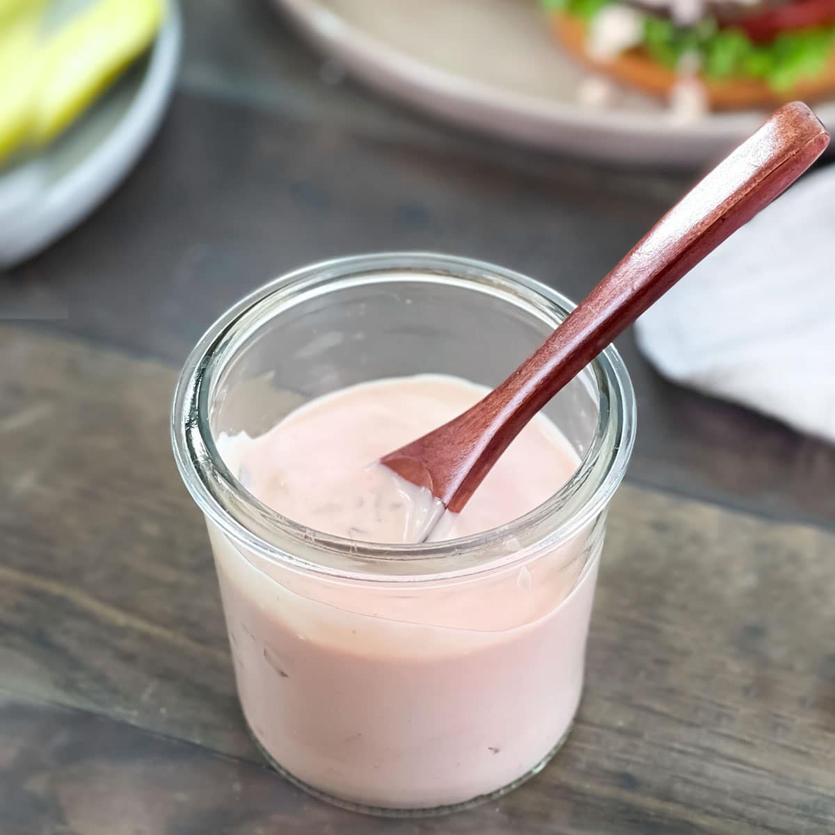 Pinkish burger sauce in a glass jar with a small wooden spoon.