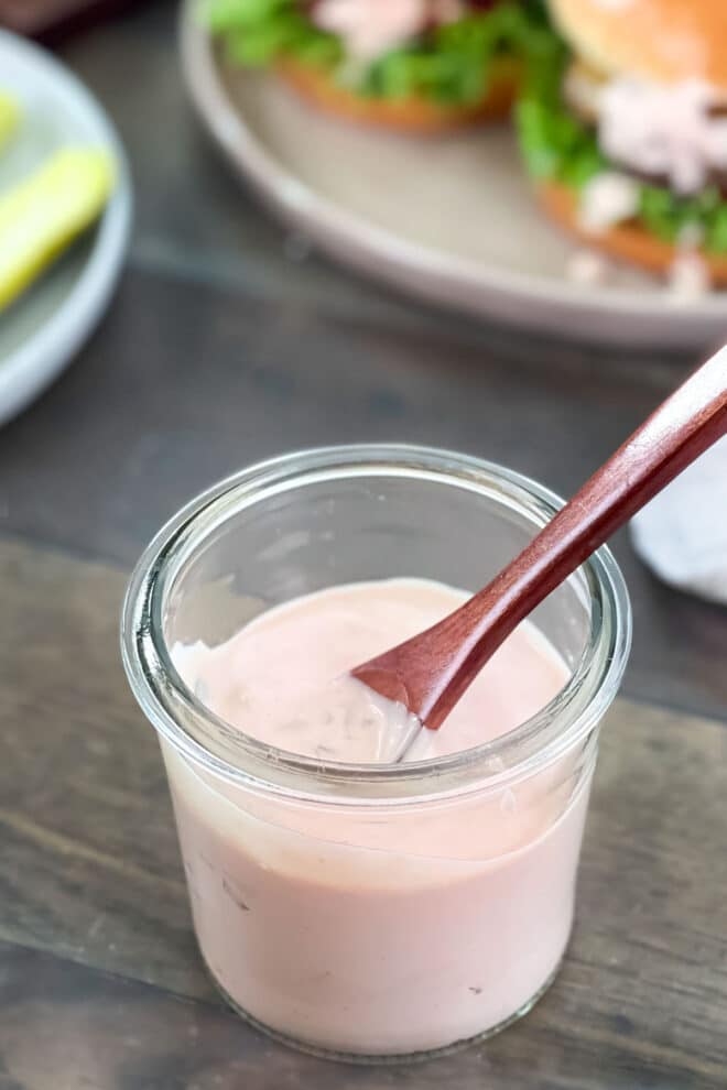 Pinkish burger sauce in a glass jar with a small wooden spoon.