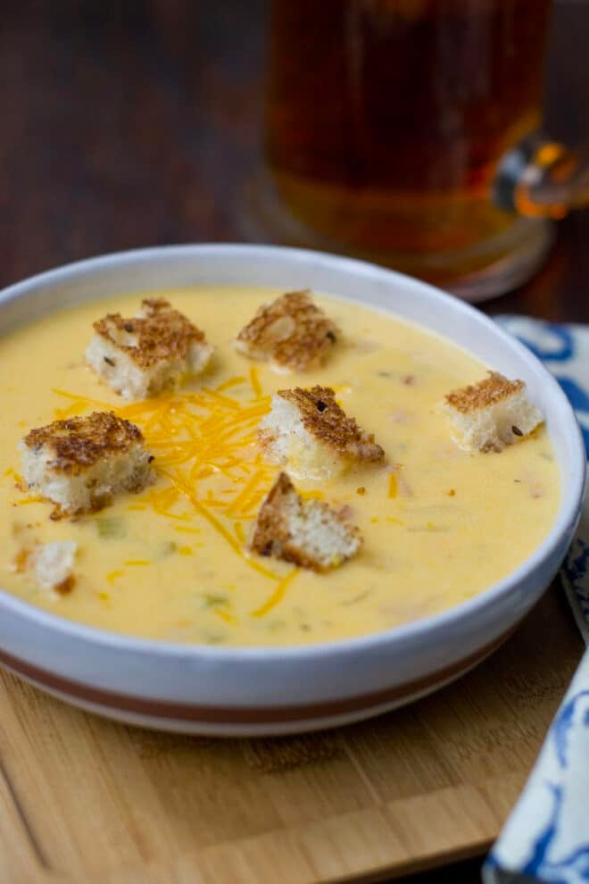 Bowl of beer cheese soup with croutons and shredded cheese on top.