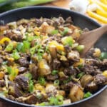 Ground Beef and Potatoes in skillet topped with cheese and green onion.