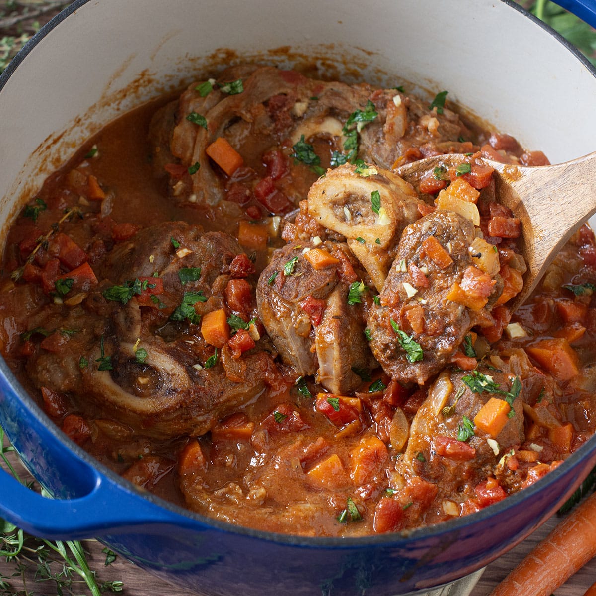 Veal Osso Buco in a large blue pot with wooden spoon.