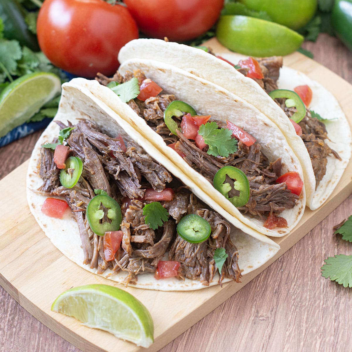 Shredded beef tacos with jalapeno and tomato with lime wedges.