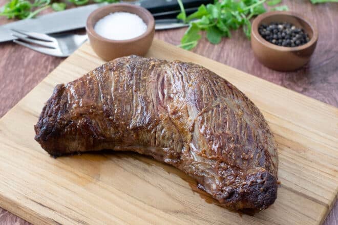 Whole cooked tri-tip steak on a wooden board.