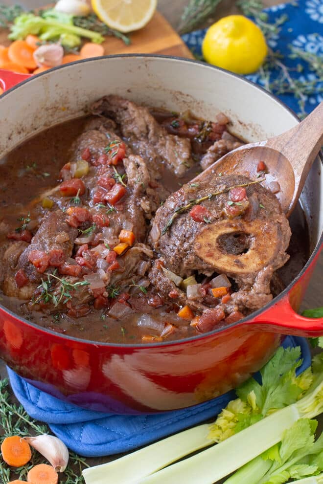 Red Dutch oven with braised beef shanks and wooden spoon.