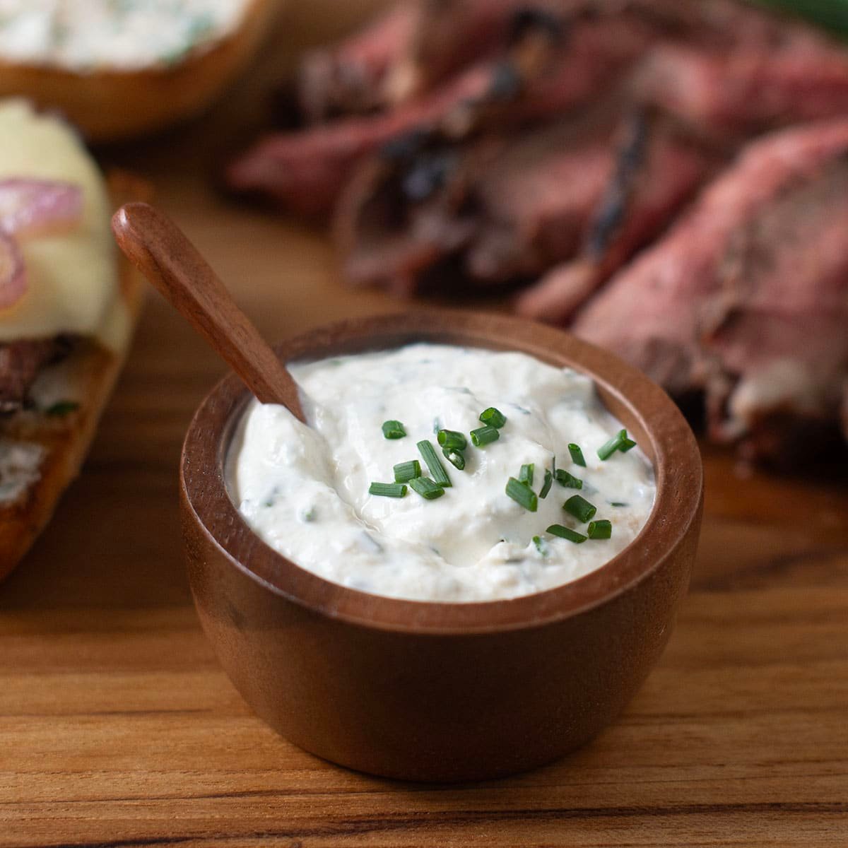 Small wooden bowl of homemade horseradish sauce with sliced tri-tip and beef sandwich in background.