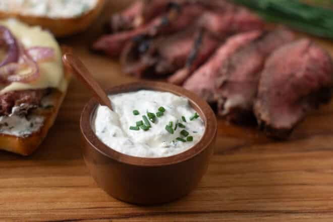 Small wooden bowl of homemade horseradish sauce with sliced tri-tip and beef sandwich in background.