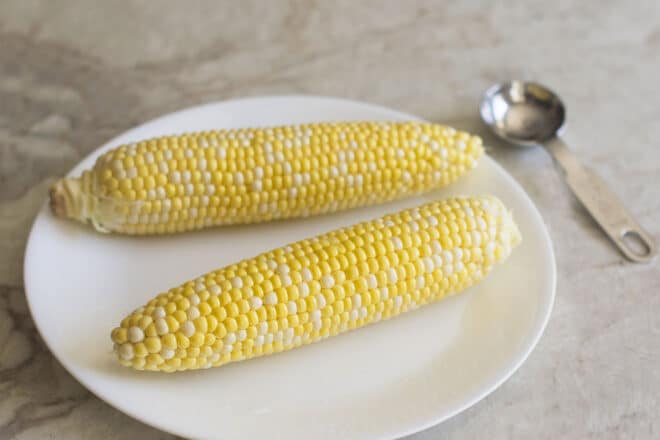 Two uncooked cobs of corn on a white plate
