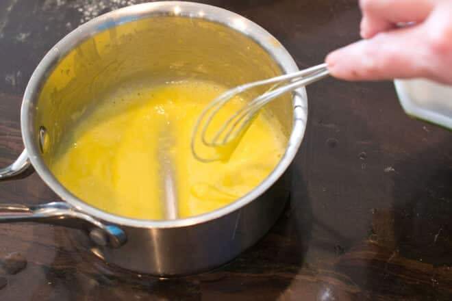 Testing egg yolk mixture thickness by dragging whisk across bottom of pan.