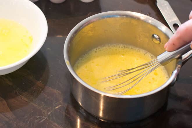 Frothing egg yolks in a saucepan with a whisk.
