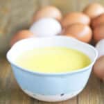 Hollandaise sauce in a white bowl with white and brown eggs in background.