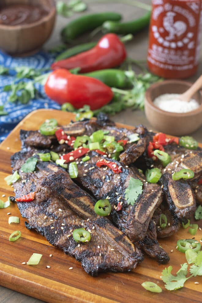 Flanken style ribs on cutting board with sliced peppers and green onion on top.