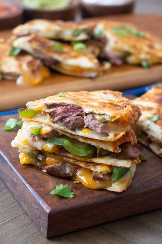 Sliced steak quesadillas with melty cheese and peppers and onions on a wooden board.