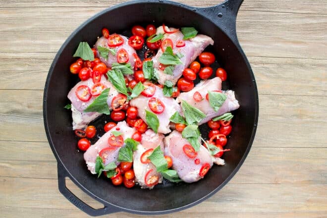 Skillet of raw chicken, tomatoes, and fresh basil.