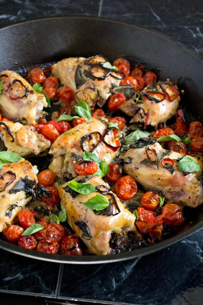 Skillet of cooked chicken, tomatoes, and fresh basil.