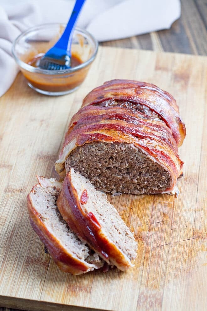 Bacon-Wrapped Meatloaf partially sliced on cutting board.