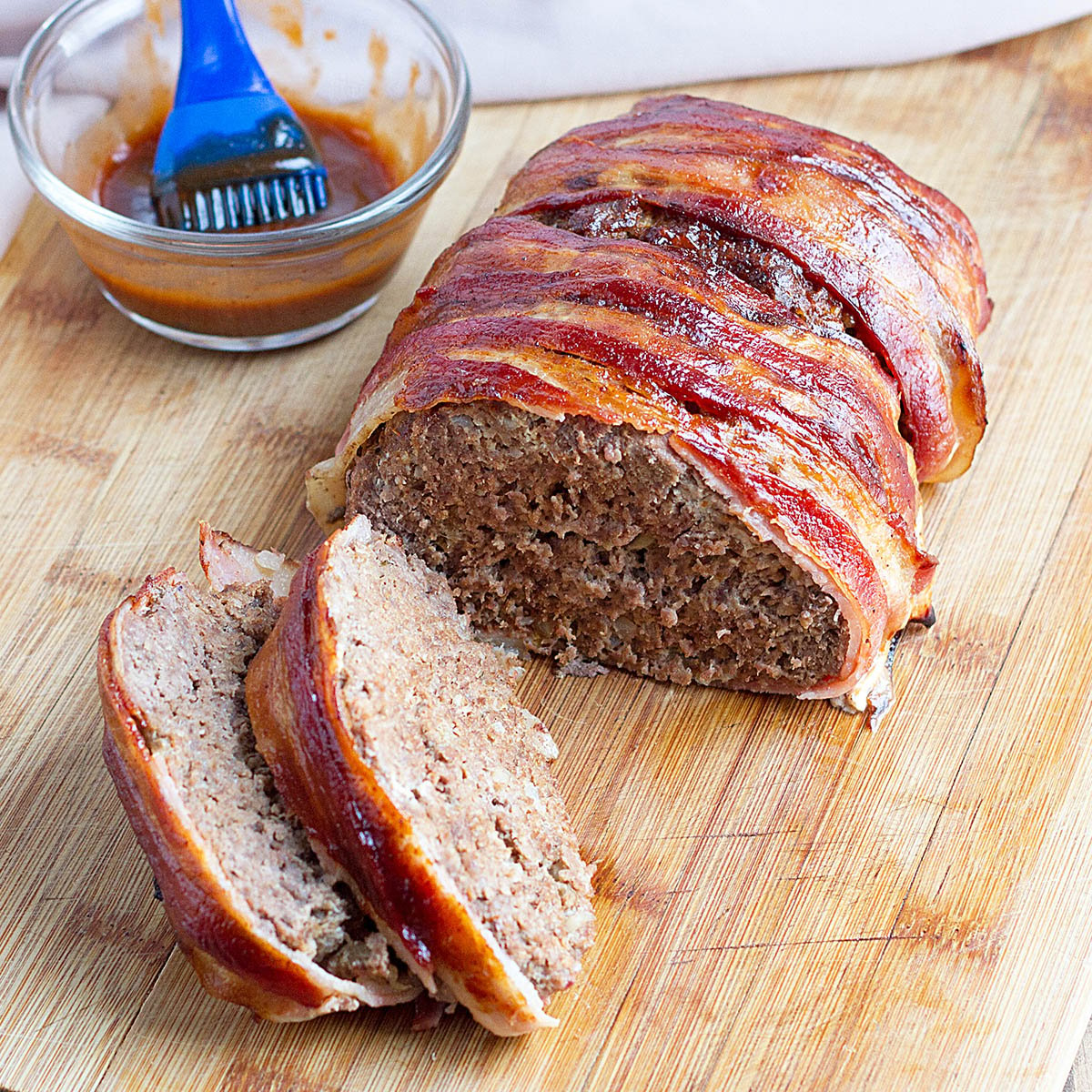 Bacon-Wrapped Meatloaf partially sliced on cutting board.