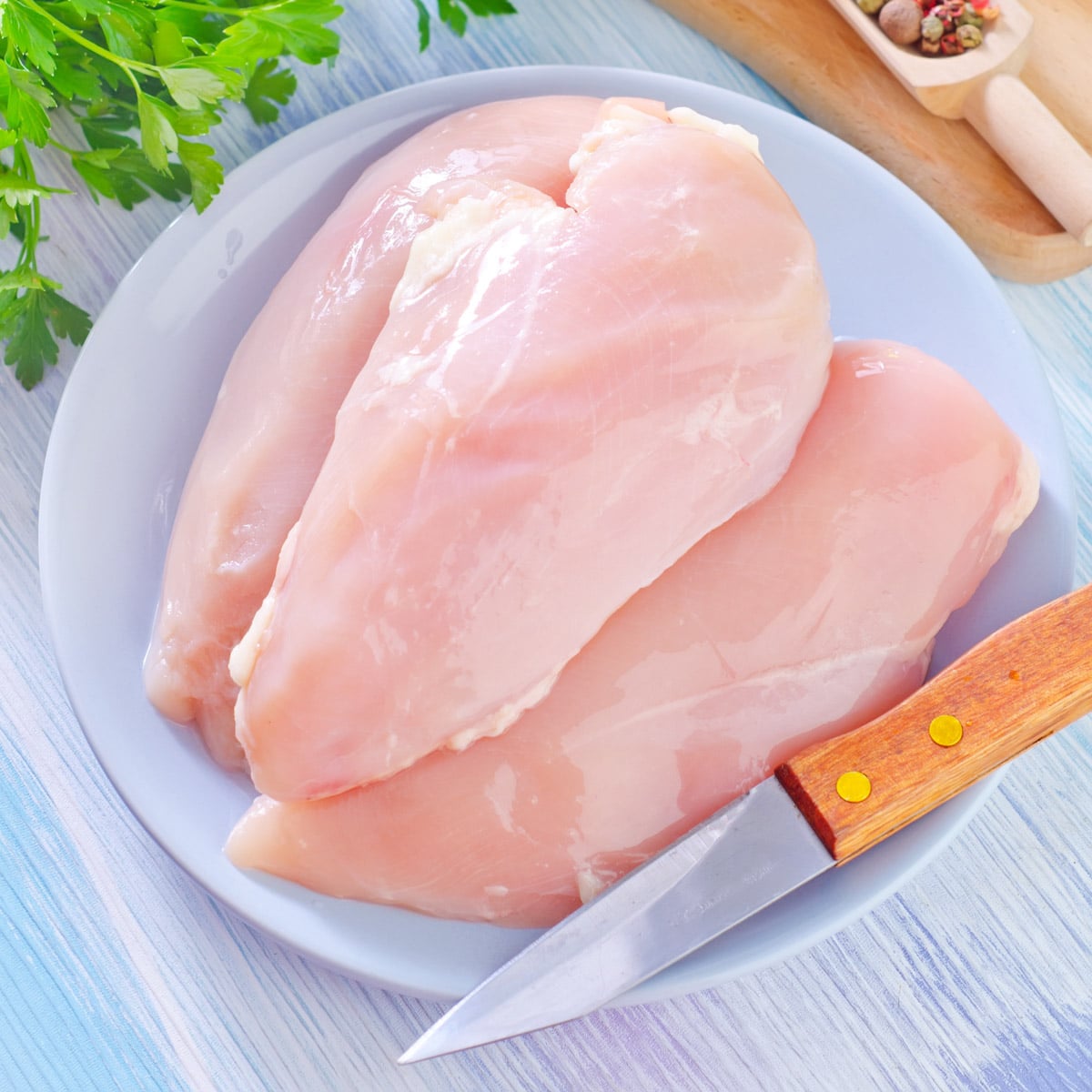 Raw chicken breasts on a plate with various aromatics around.