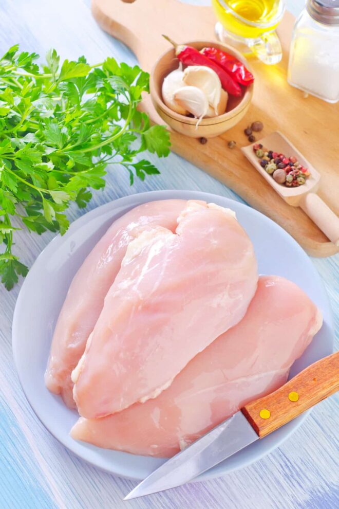 Raw chicken breasts on a plate with various aromatics around.