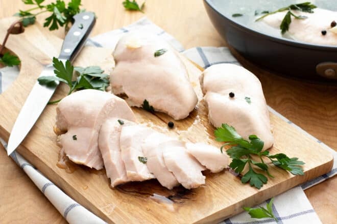 Poached chicken breasts sliced on a cutting board.