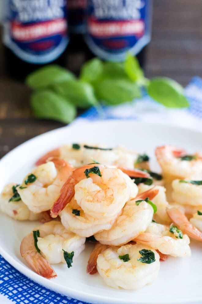 White plate with cooked shrimp with bits of basil.